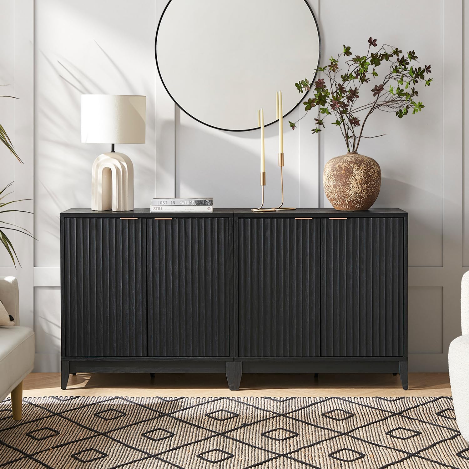 A black textured buffet cabinet styled with modern accessories, including a table lamp, tall candles, and a circular mirror.