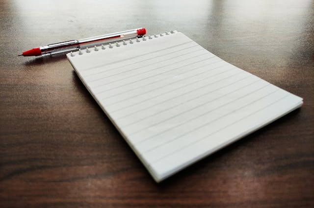 A notepad and a red pen sitting on table