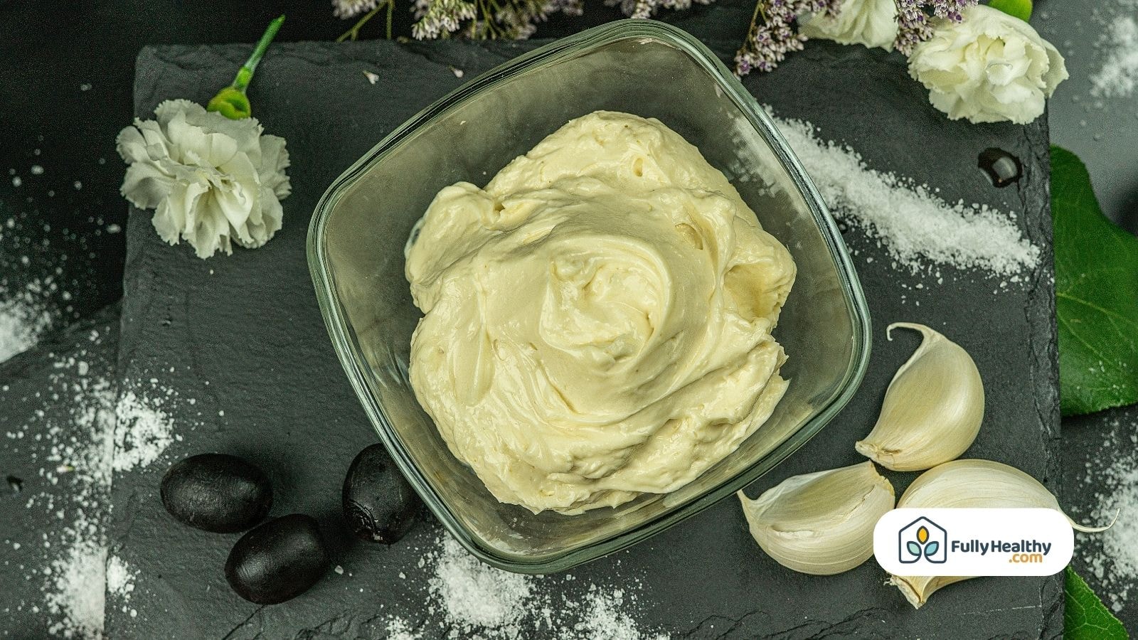 Homemade mayonnaise in glass bowl with garlic and black olives