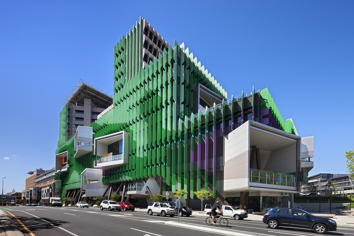 The angular, multi-story building boasts a bold green facade with purple accents and large white jutting sections, embodying innovative hospital design.