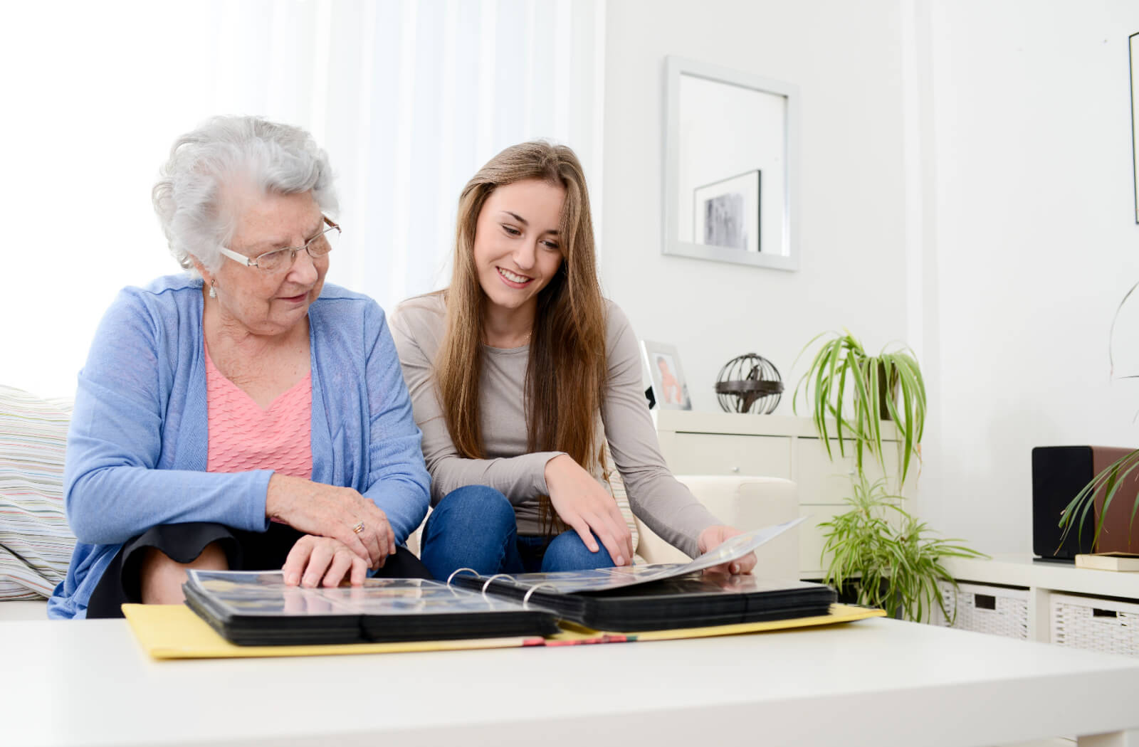 An older adult in memory care during a visit with their grandchild looking through a photo album and reminiscing.