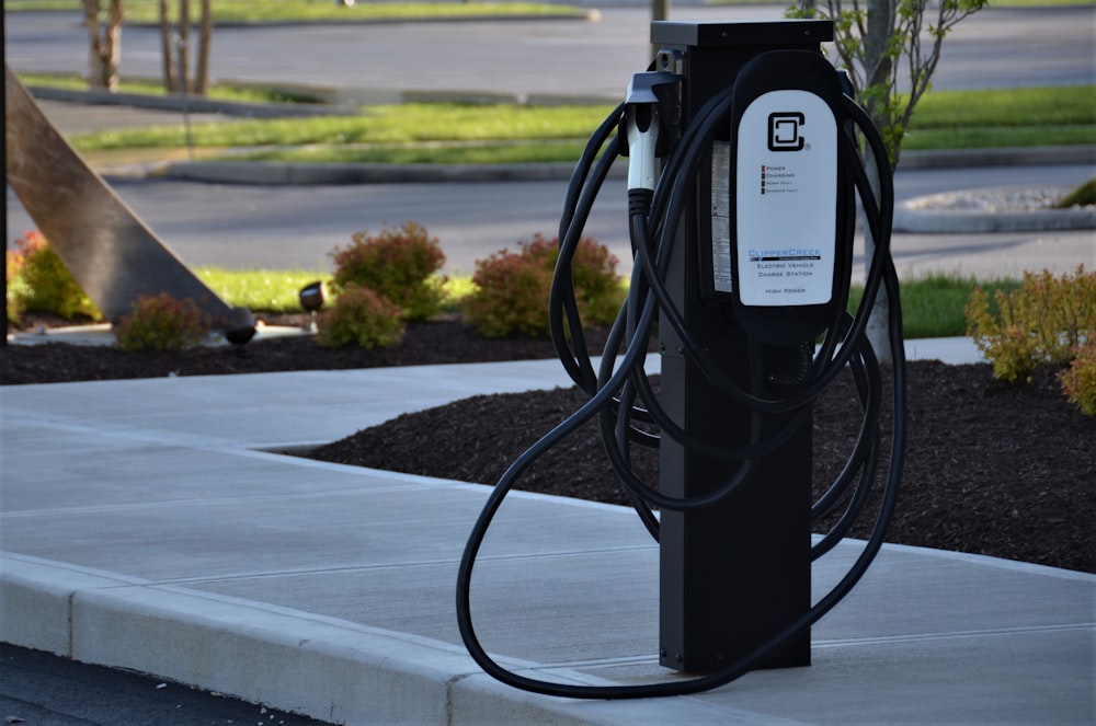 An electric vehicles charger. black metal stand on grey concrete road during daytime 