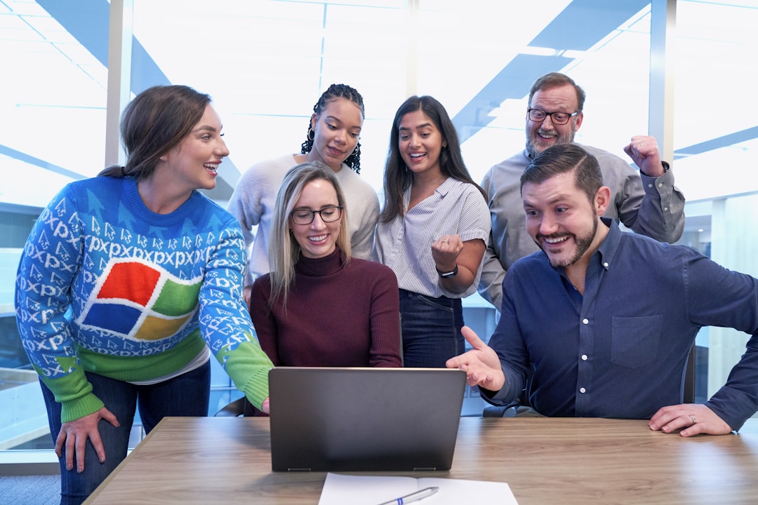 Professionals in an office gathered around a table with a laptop, collaborating on telephony software