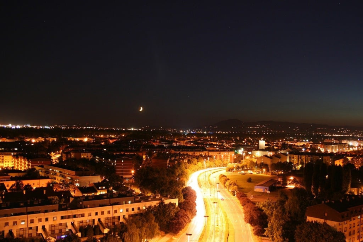 It's dark and road is lighting and moon in the sky 
