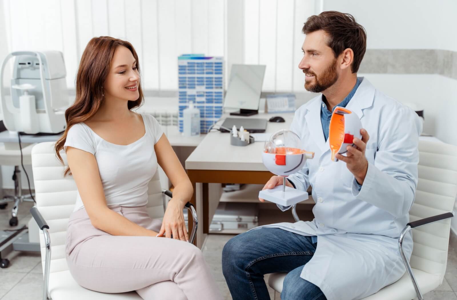 An optometrist uses an anatomical model of the eye to explain the difference between glaucoma and AMD to a patient.