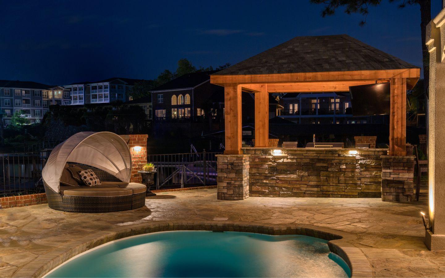 A pool with a gazebo and a gazebo at night

Description automatically generated