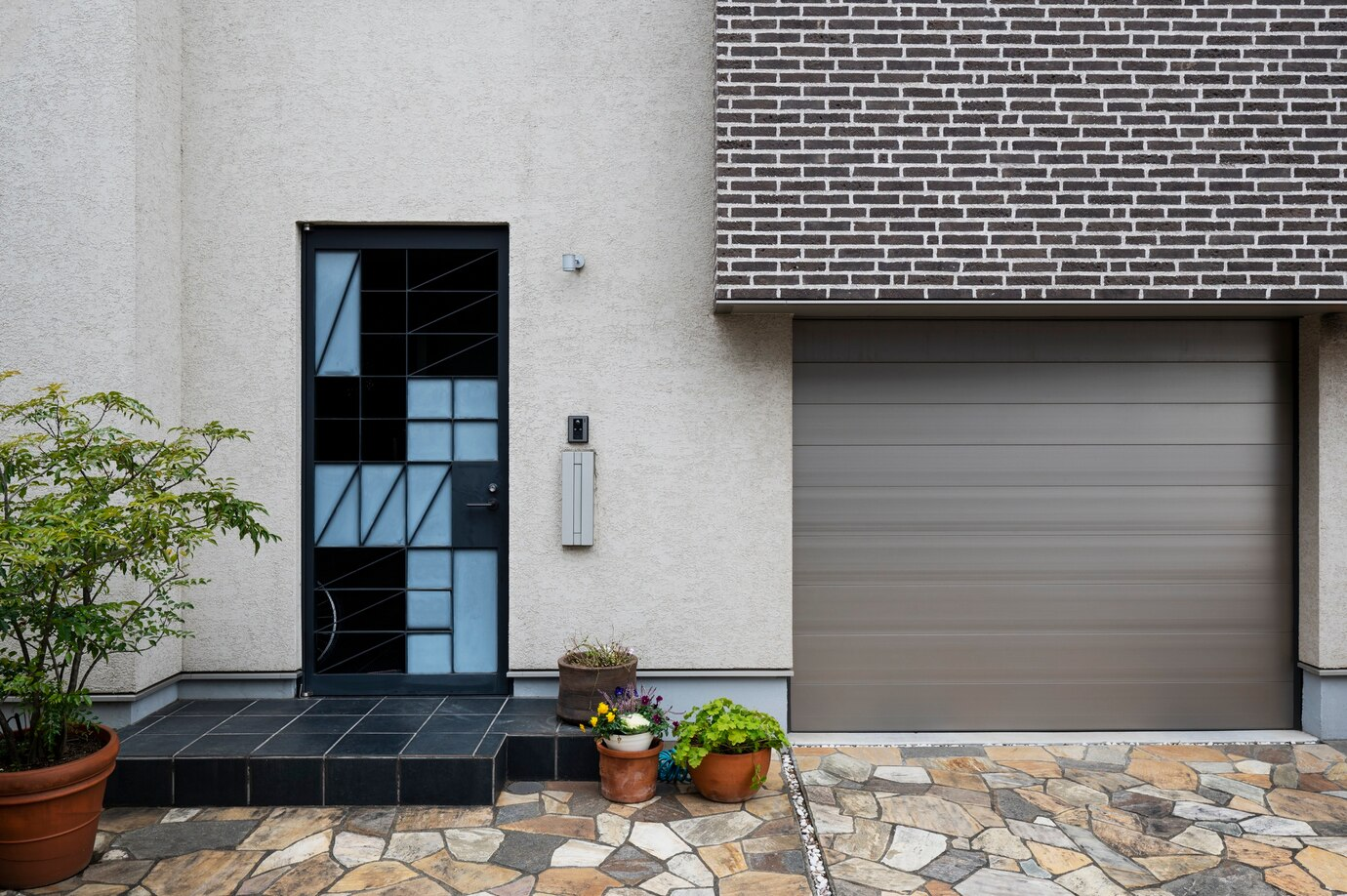 a modern home featuring a steel garage door and a stylish front door with geometric patterns and frosted glass panes. The design combines functionality with aesthetic appeal