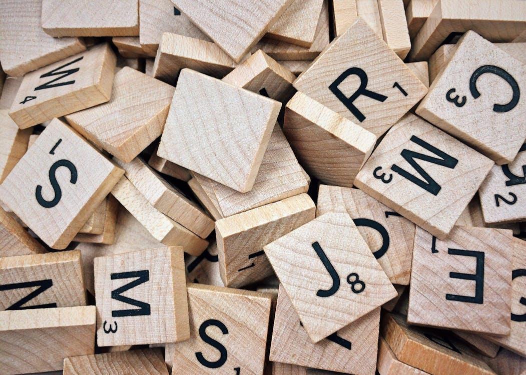 Free A collection of wooden Scrabble tiles with letters and numbers stacked randomly. Stock Photo