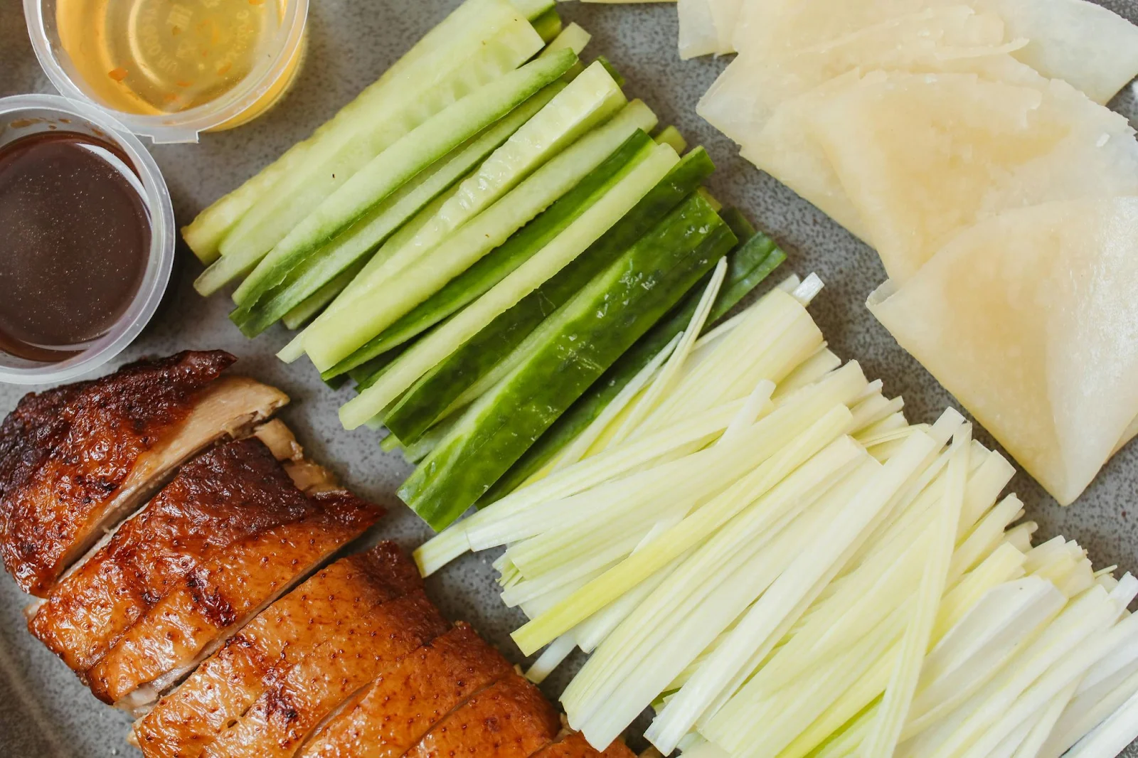 peking duck recipe in a plate with lot of veggies and sauces and oil in a cup.