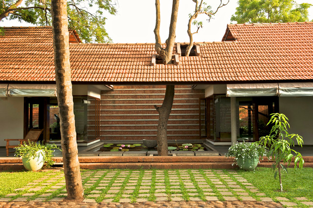 A serene courtyard with a red-tiled roof house, showcasing traditional architecture with large wooden beams and an open patio.