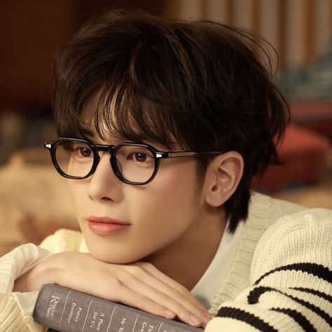 This contains an image of Taehyun with glasses is leaning on a book