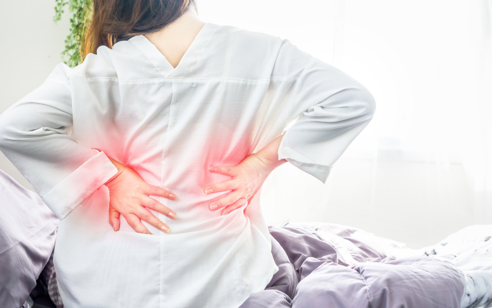 Woman experiencing lower back pain while sitting on a bed, highlighting the importance of proper mattress support for spinal health and comfort
