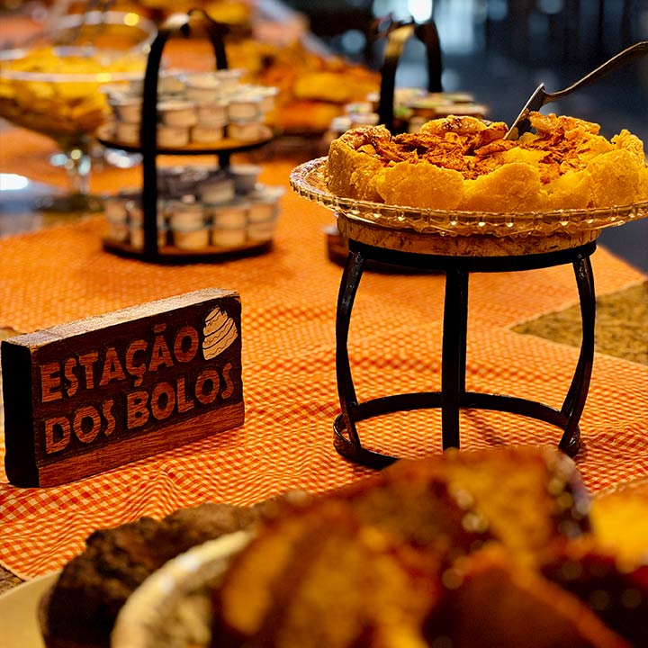 Imagem de uma estação de bolos, com uma variedade de tortas e doces dispostos em mesas decoradas, evidenciando um ambiente festivo e acolhedor para a degustação.