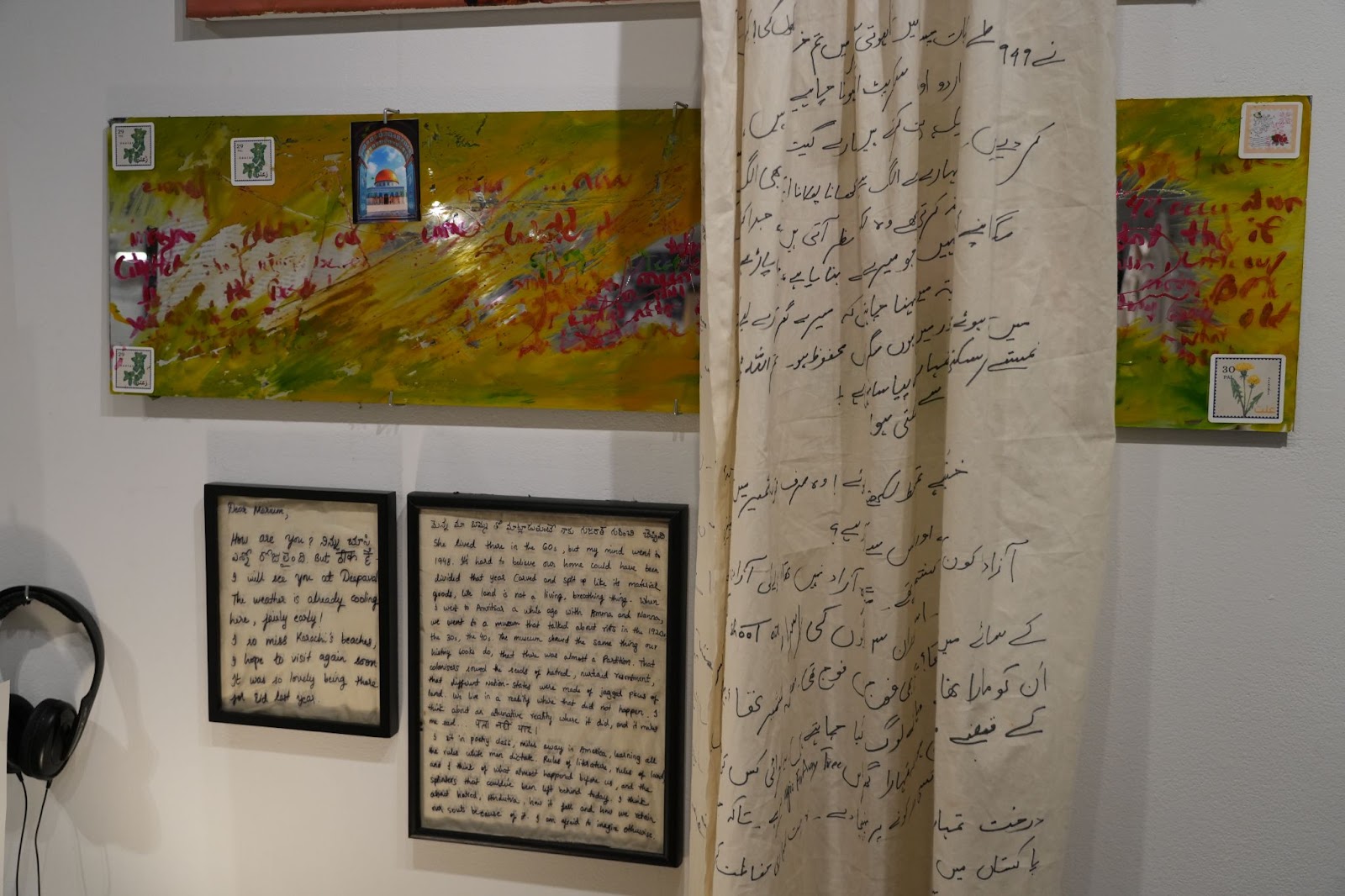 Image: Alternate view of Dreaming in Letters. Text covers a curtain hanging from the top of the frame. Other letters are framed and featured alongside the curtain. Photograph by Curators Under Censorship.  