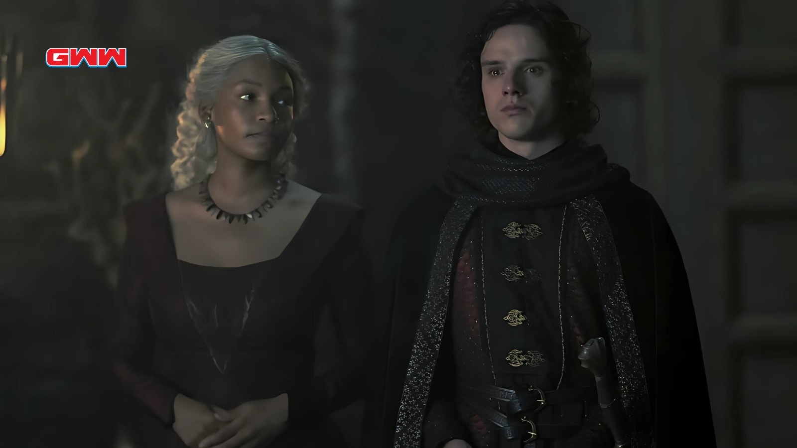 Phoebe Campbell and Harry Collett standing solemnly in dim castle hallway