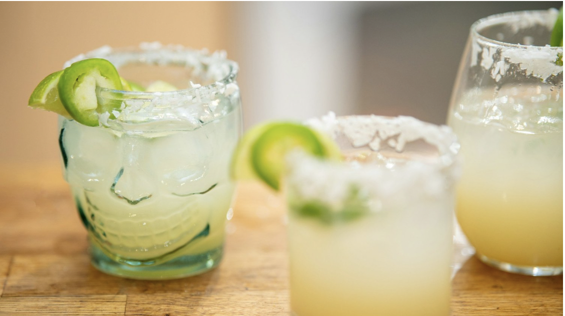 Decorative glasses are filled with margaritas with a salt rim, a lime slice, and a jalapeno