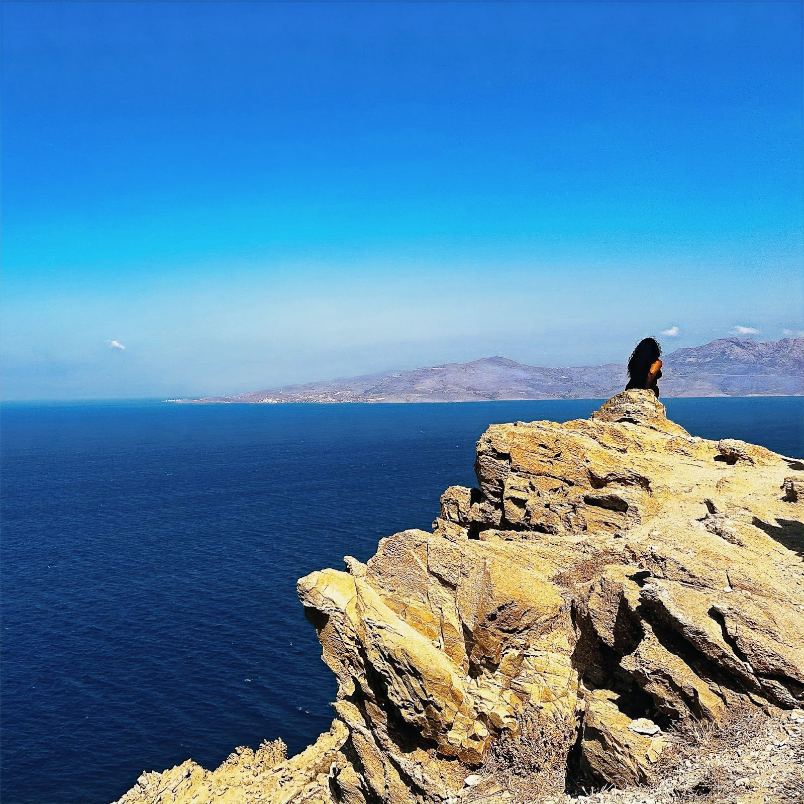 Mykonos, woman sitting on edge of cliff over water