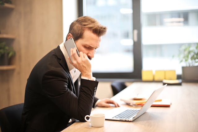 A person sitting at a laptop, taking a phone call.