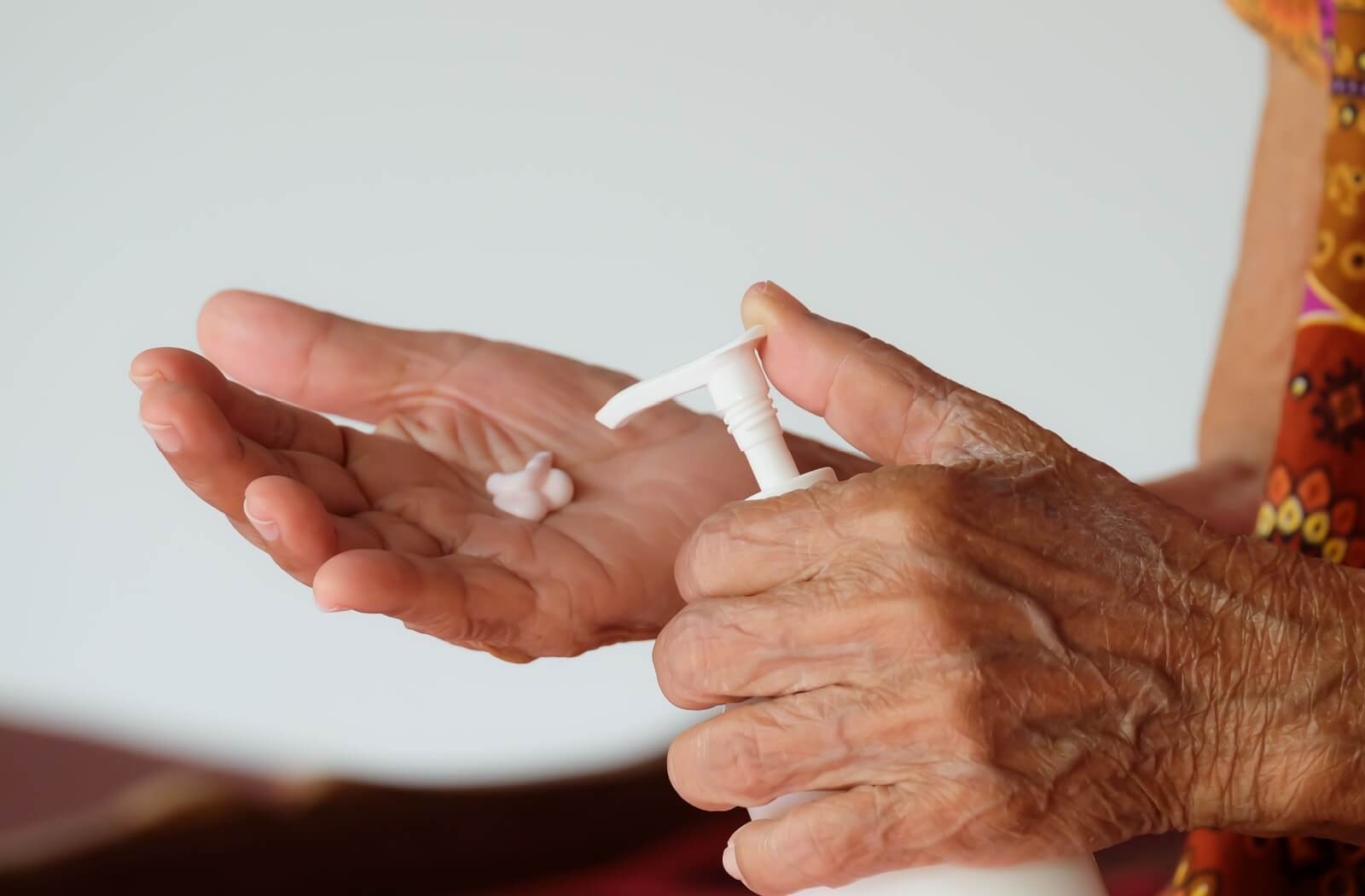 Close-up of a pair of dry hands with raised veins squirting a dollop of moisturizer onto their palms