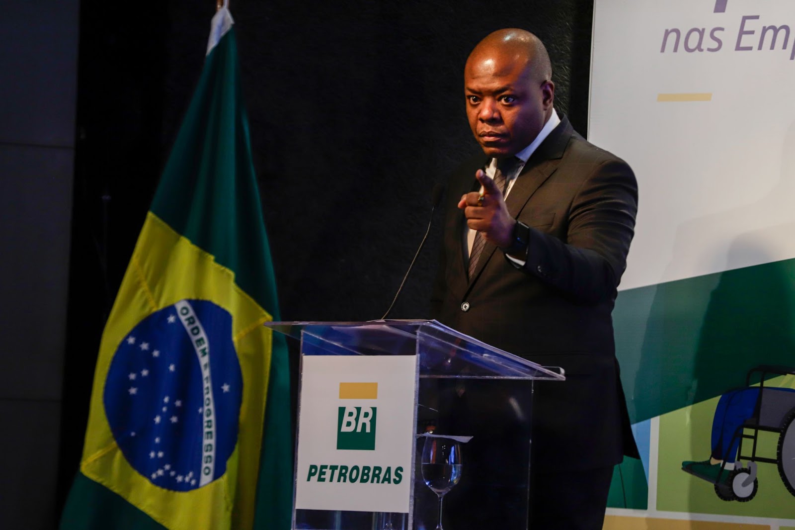 Silvio Almeida em um palanque com símbolo da Petrobrás, ao lado da bandeira do Brasil, olha sério para frente e aponta o dedo. Imagem anterior as denúncias