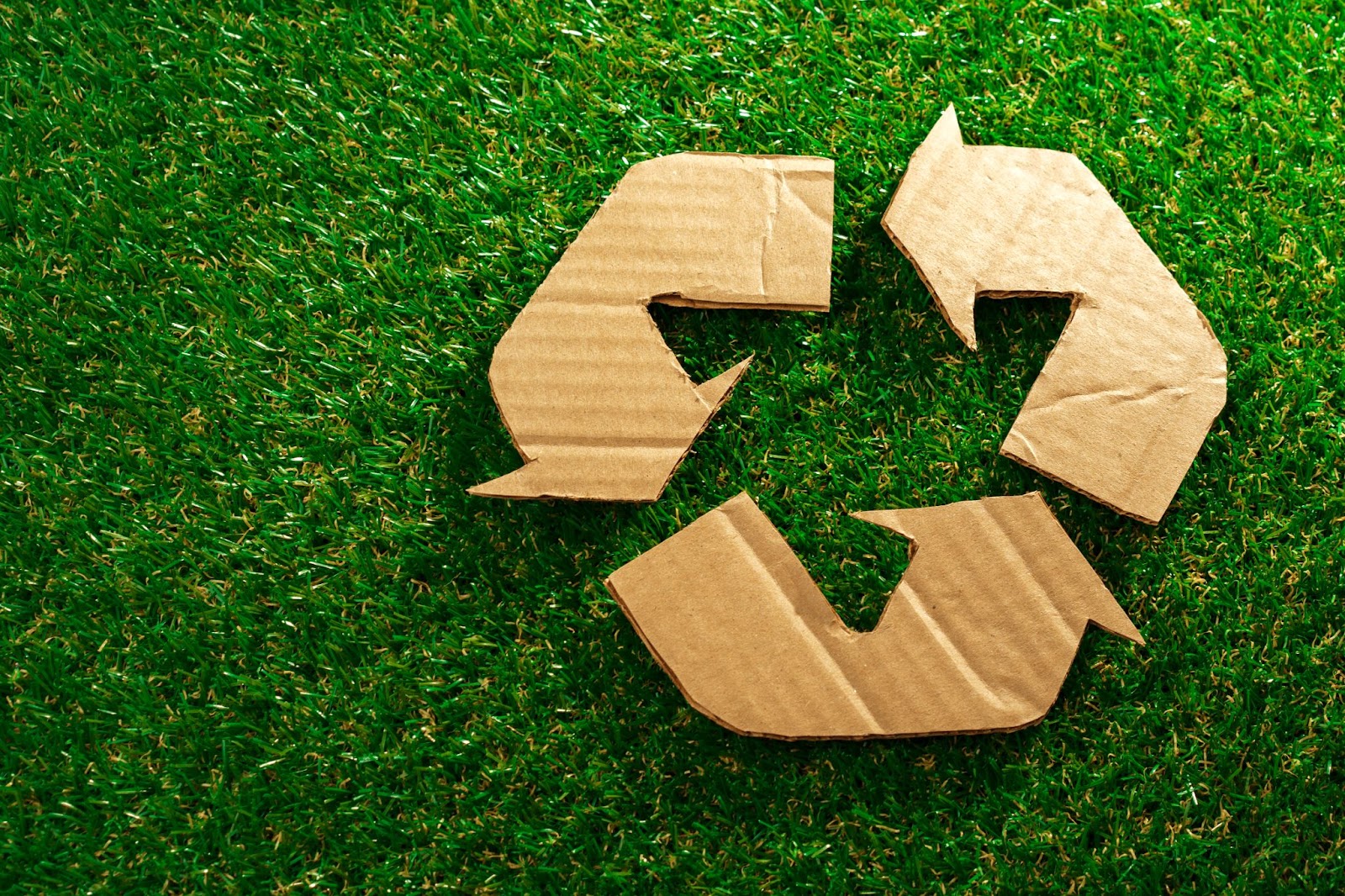 Recycling symbol made out of cardboard on a patch of grass. 