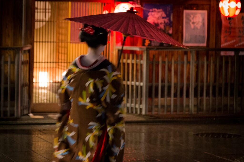 Maiko in traditional kimono walking on Hanamikoji street at night in Gion district during optimal golden hour lighting for photography