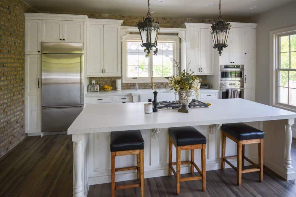 The kitchen is equipped with stainless steel appliances, white cabinetry, and a breakfast island lined with leather cushioned stools.