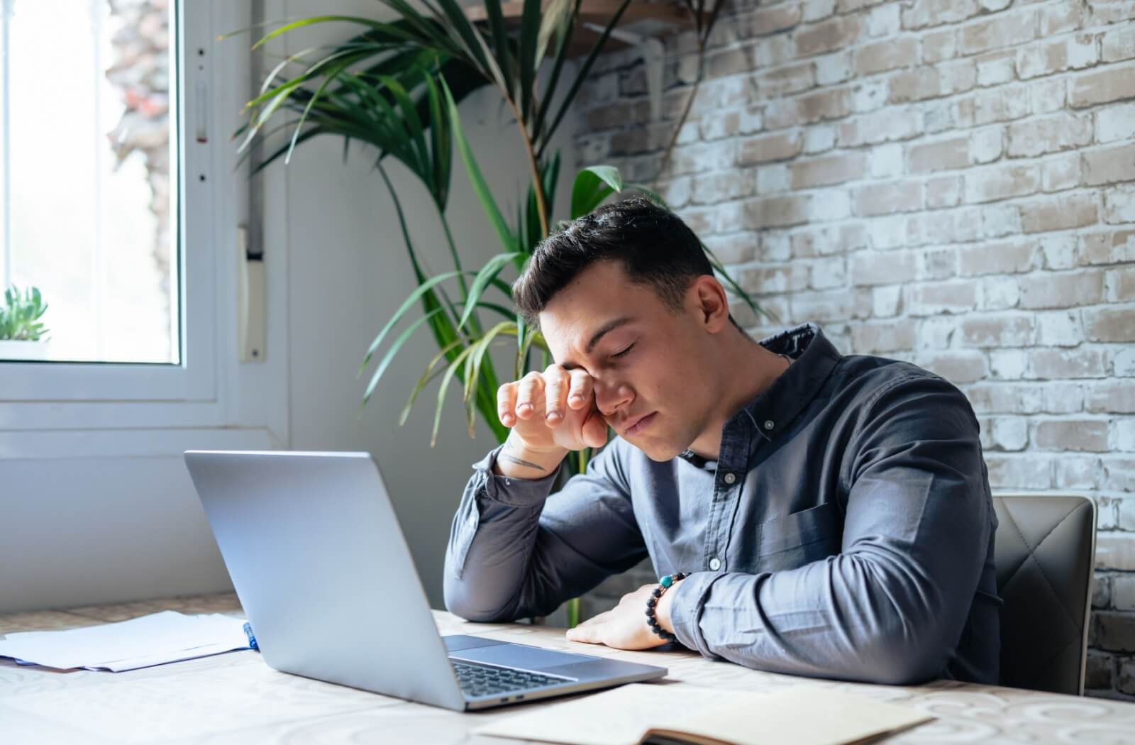 A teenaged boy rubs his sore eyes while sitting in front of a computer trying to do schoolwork.