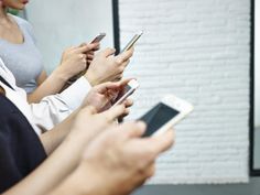 This contain four people are using their cell phones in a row 