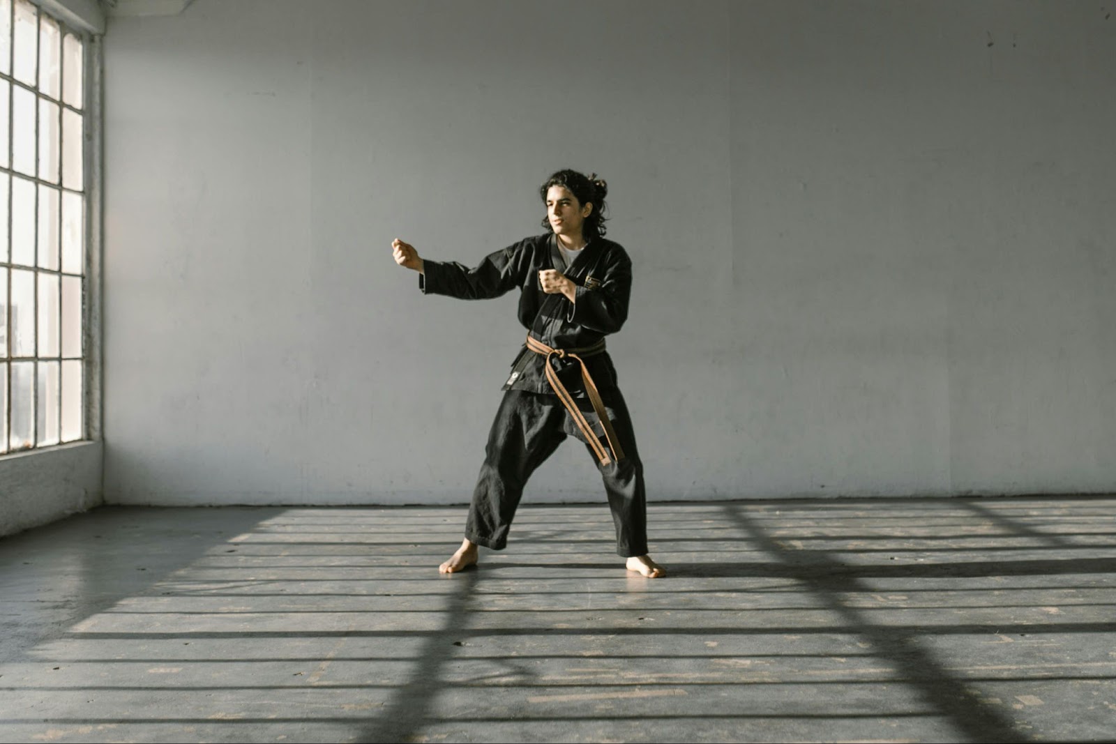 A female martial arts student stands in a fighting stance, focused and ready, with her hands raised for defense and her feet positioned for balance during training.