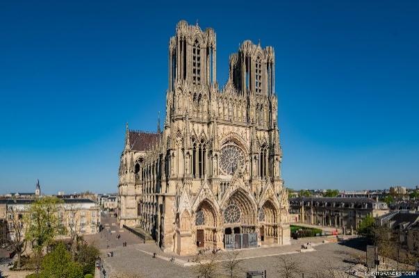 A large stone building with many windows with Reims Cathedral in the backgroundDescription automatically generated