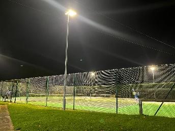 A tennis court with lights on Description automatically generated