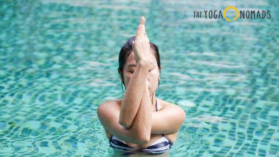 Aqua Yoga: An individual practicing yoga in a body of water, with their hands together above their head.