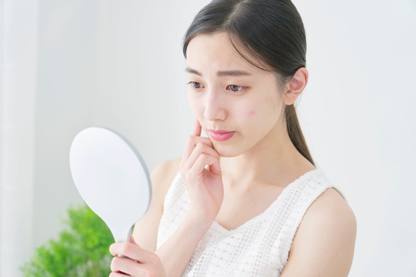 A person holds a small mirror and looks concerned as they examine the dry skin around their eyes.