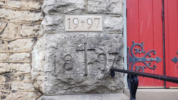 A stone wall with numbers and a cross carved into it

Description automatically generated