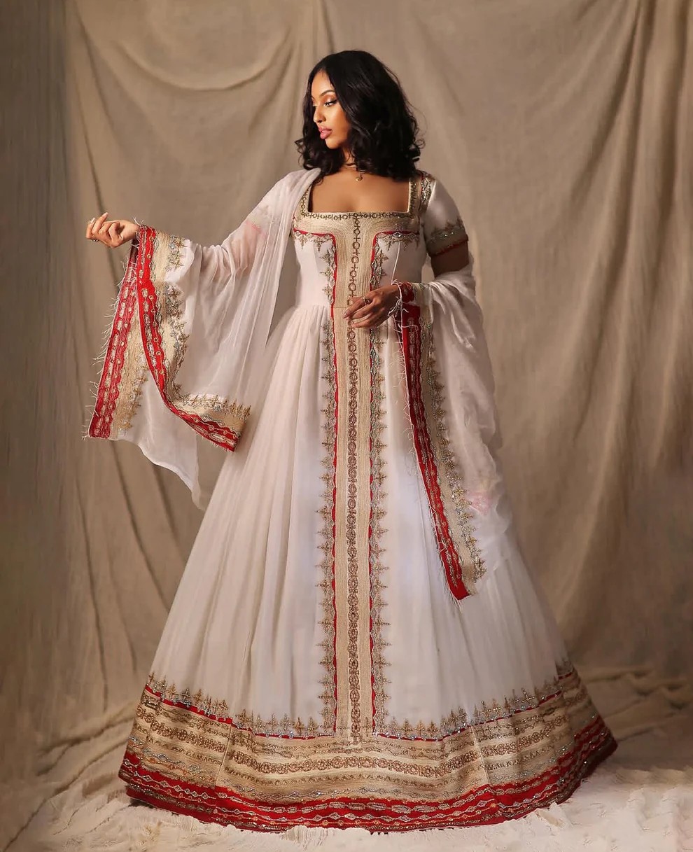 Woman wearing a classic white Habesha kemis with gold embroidery and red accents