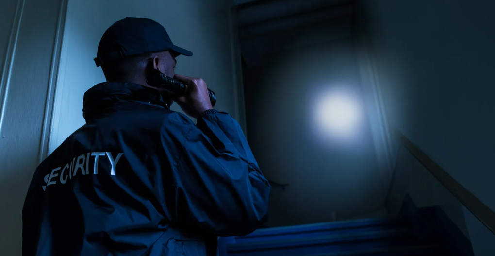 (A nighttime security guard patrols a dark stairwell with a flashlight, emphasizing the importance of vigilant 24/7 protection in low-light and high-risk areas.)