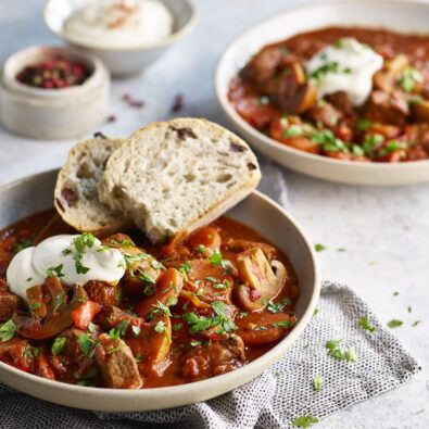 Two bowls of traditional Hungarian goulash, topped with sour cream and herbs, served with slices of bread.