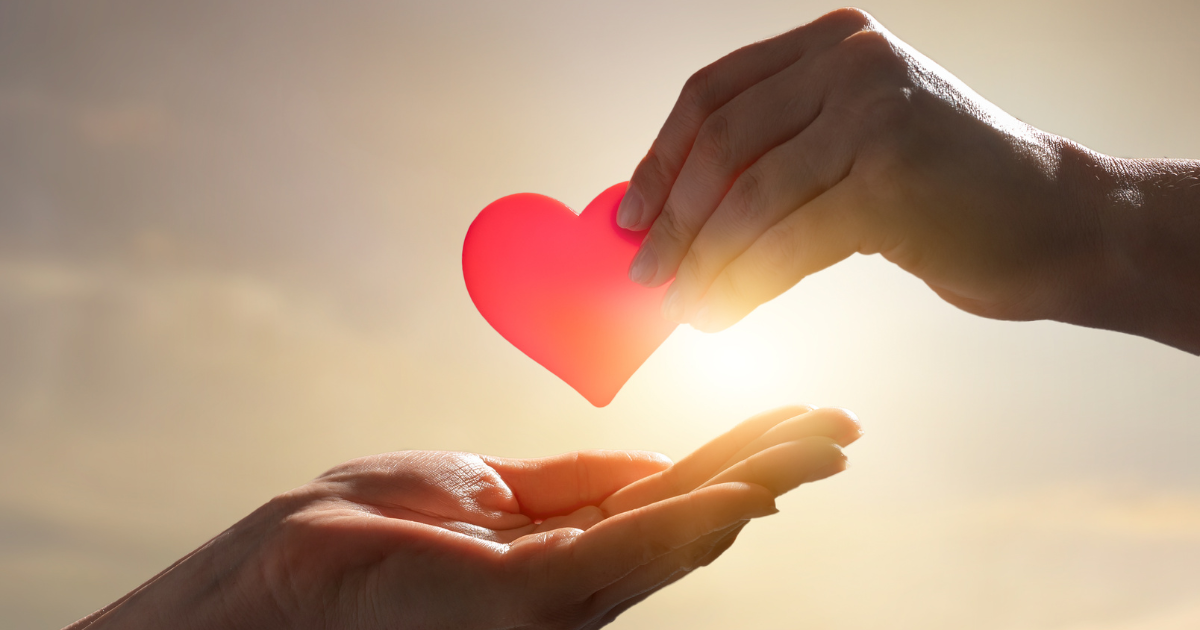 A hand giving another hand a red paper heart.