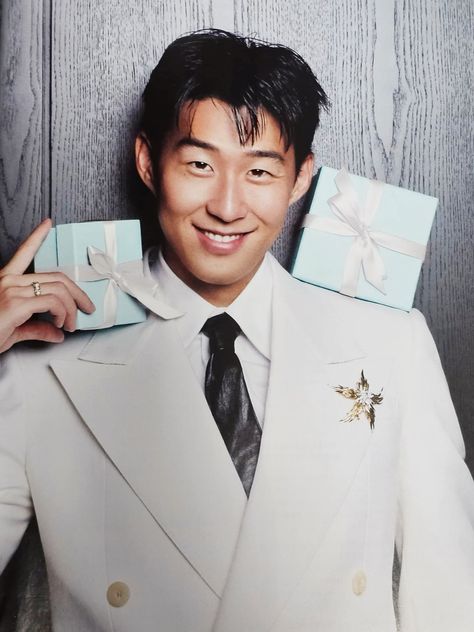 This  contain Son Heung Min  in a suit and tie holding two small boxes on his shoulders, both with bows