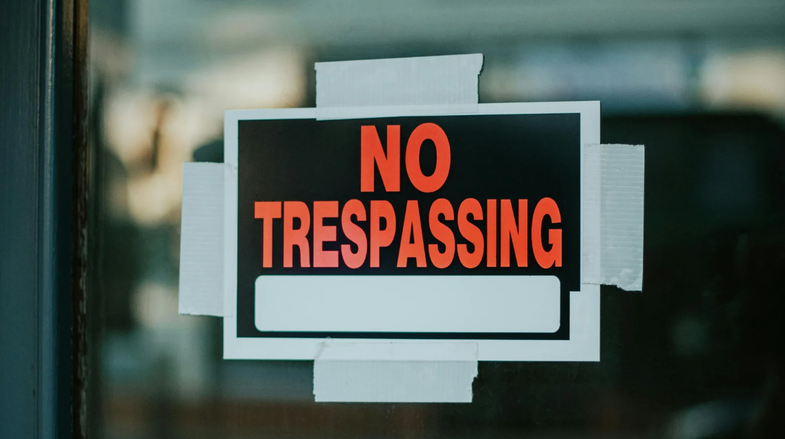 (Close-up of a bold “No Trespassing” sign taped to a glass door, symbolizing property boundaries and potential legal implications for unauthorized entry.)