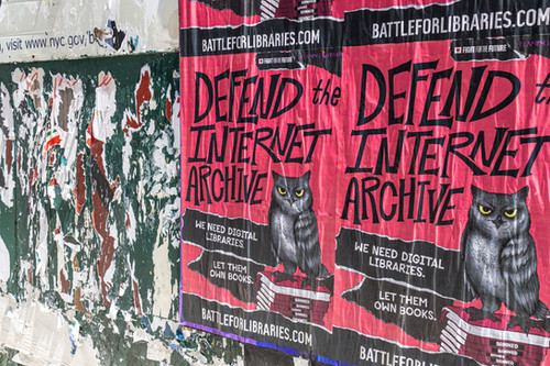 Posters reading "defend the Internet Archive" are wheatpasted on a wall.