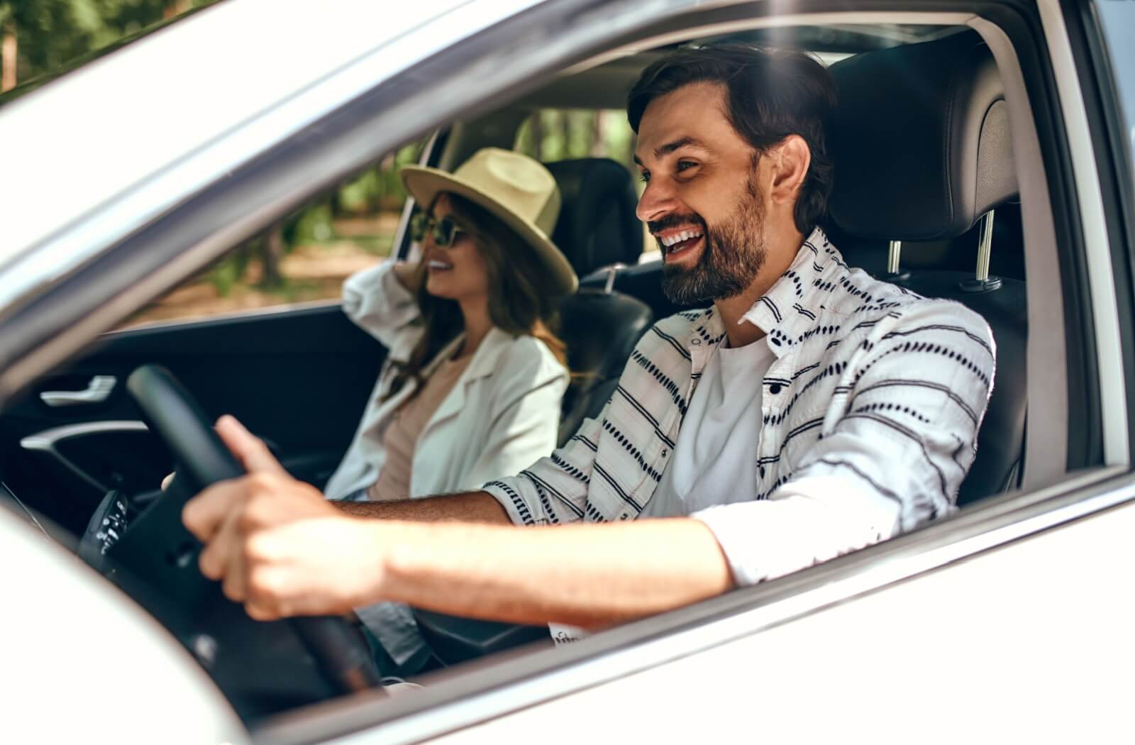 A woman getting a ride home from her friend after an eye dilating exam, wearing a sunhat & sunglasses to help protect her eyes.