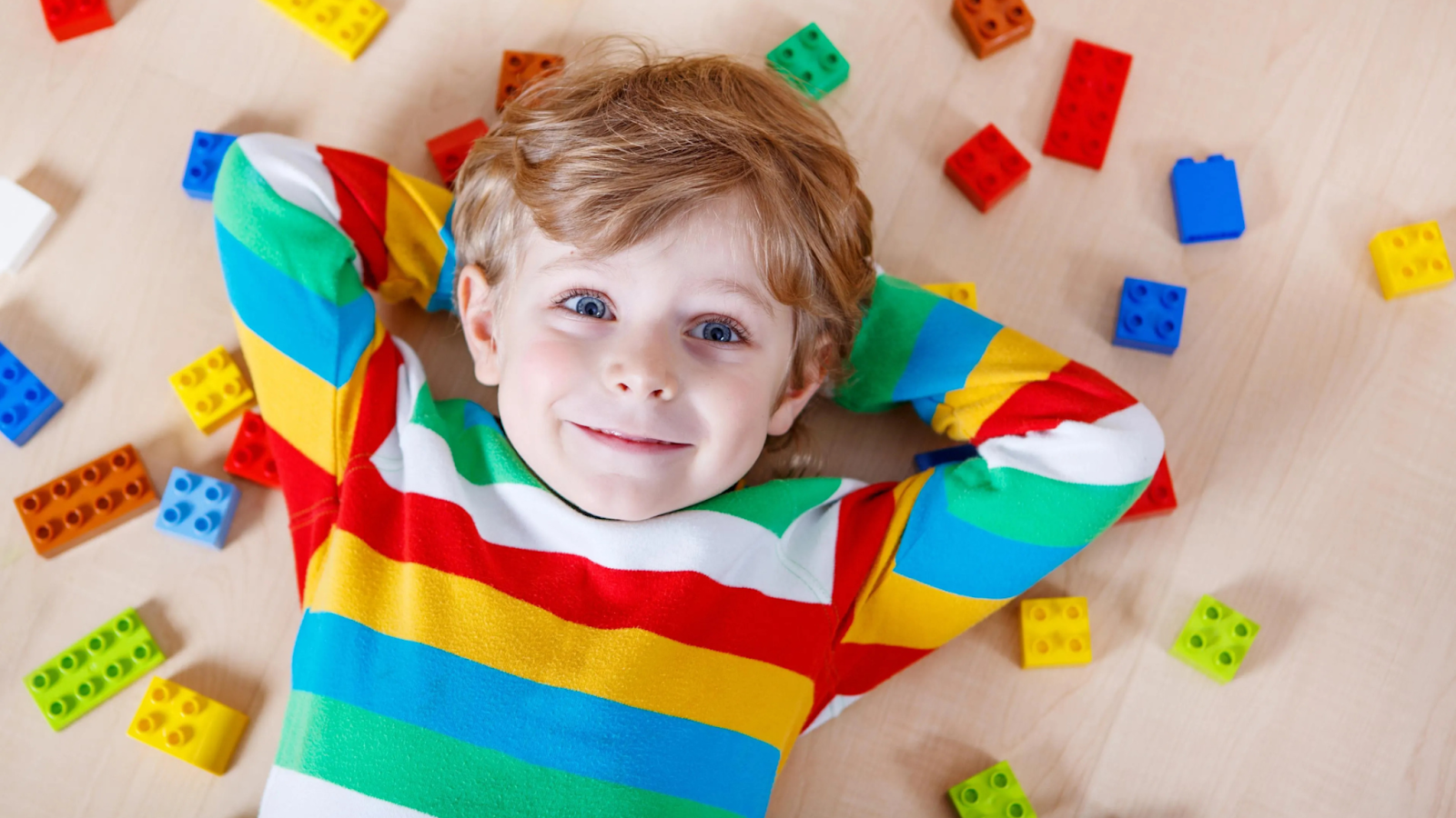Happy child lying on the floor with colorful building blocks, enjoying a creative game for kids | Royal Ramakra.