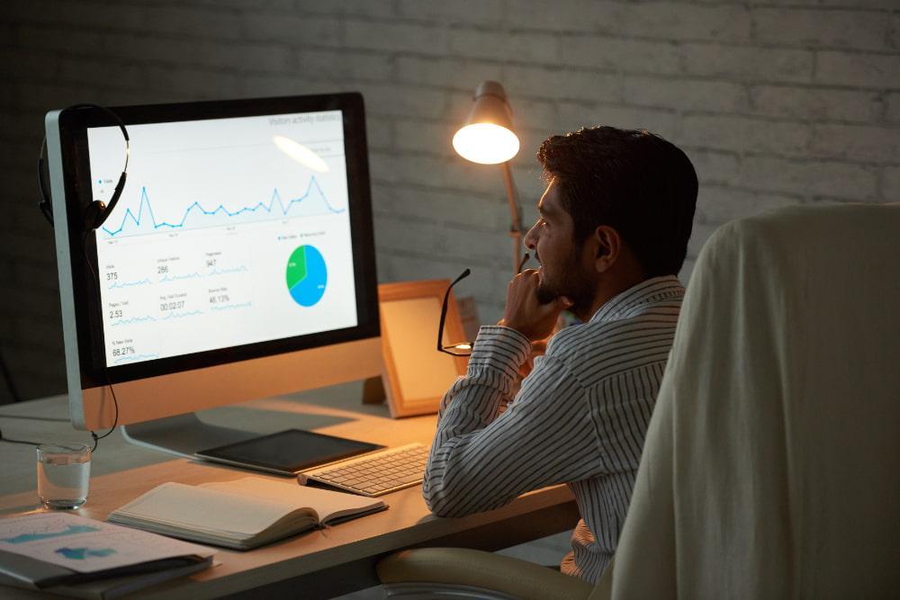 Man reviewing charts and data on a computer screen while working in an office.