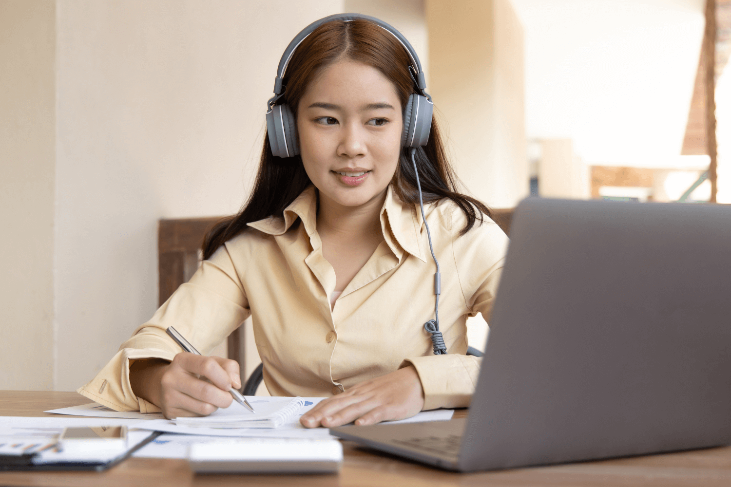 woman wearing headphones while browsing on her computer and taking notes