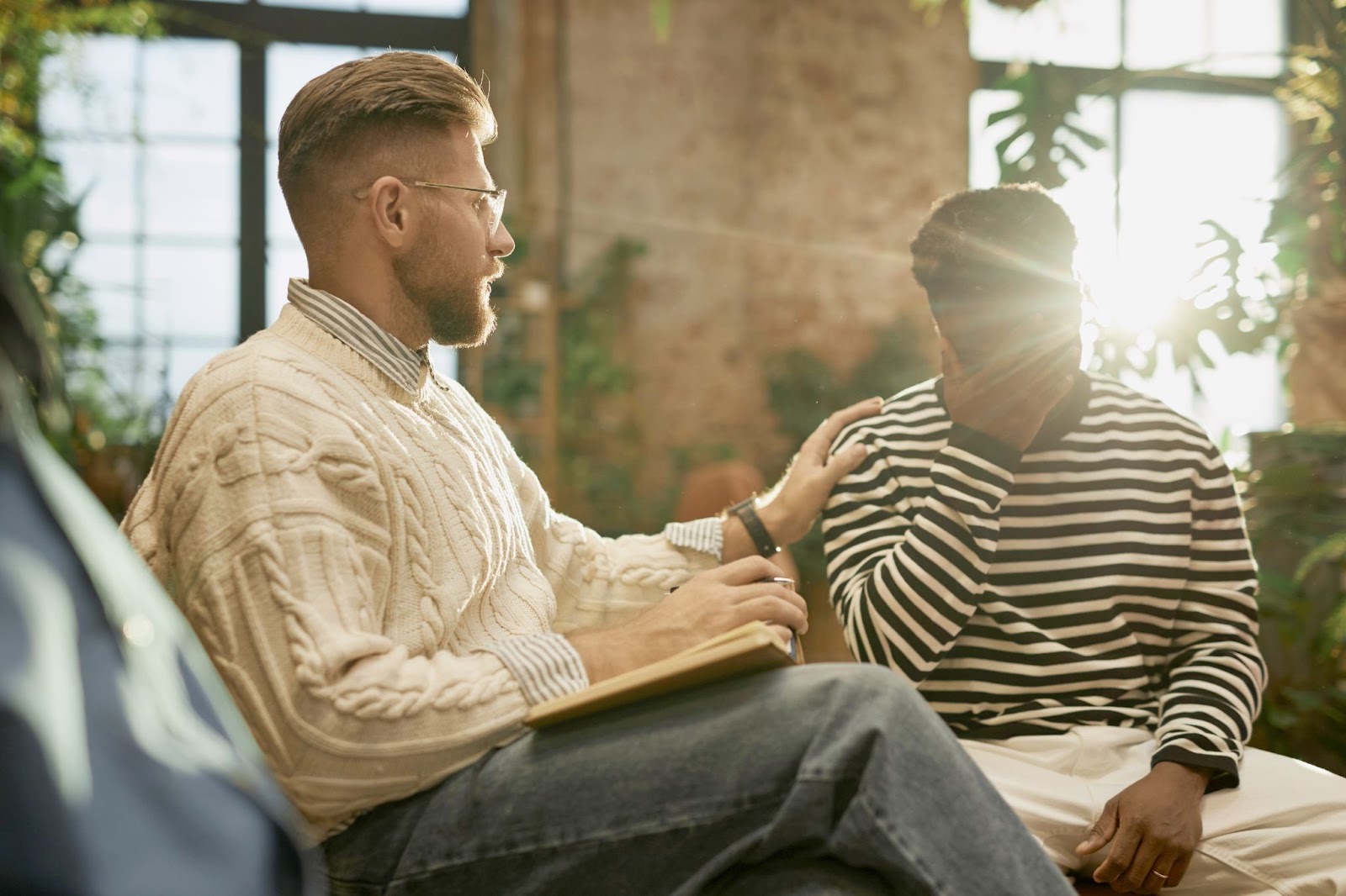 A male psychologist is next to a man with his hand over his face.