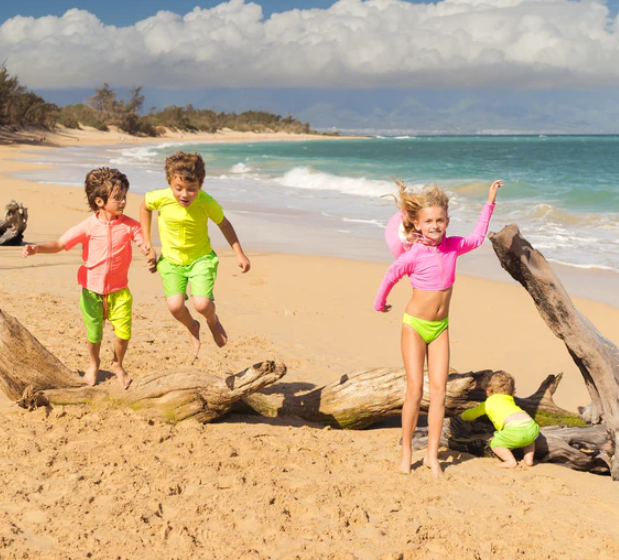 Kids jumping at the beach in neon-colored protective swimwear by SwimZip—10 ways to keep your kids safe during summer vacation