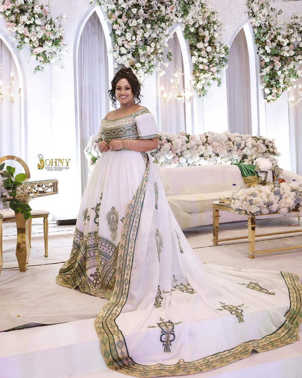 Bride in white wedding Habesha dress with green and gold embroidery at a decorated wedding venue
