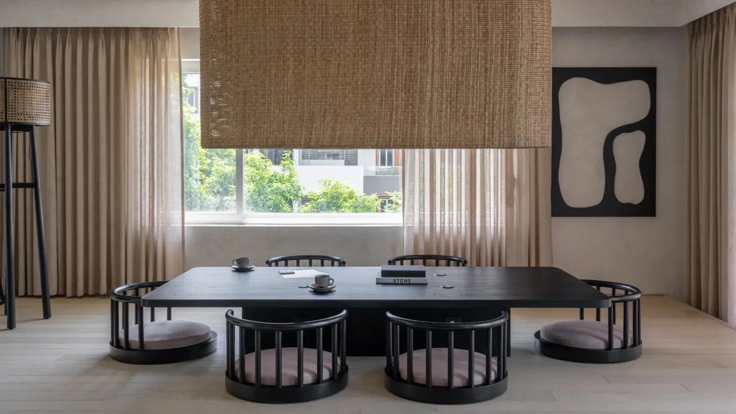 A minimalist dining room features a low rectangular black dining table with five round black chairs with cushions around it.